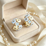 These 18k gold-plated stud/clip earrings feature delicate blossoms crafted with enamel glaze and inlaid with sparkling zircon stones. The combination of soft blue, creamy yellow and lustrous gold creates a romantic and feminine look that captures the essence of blooming florals.