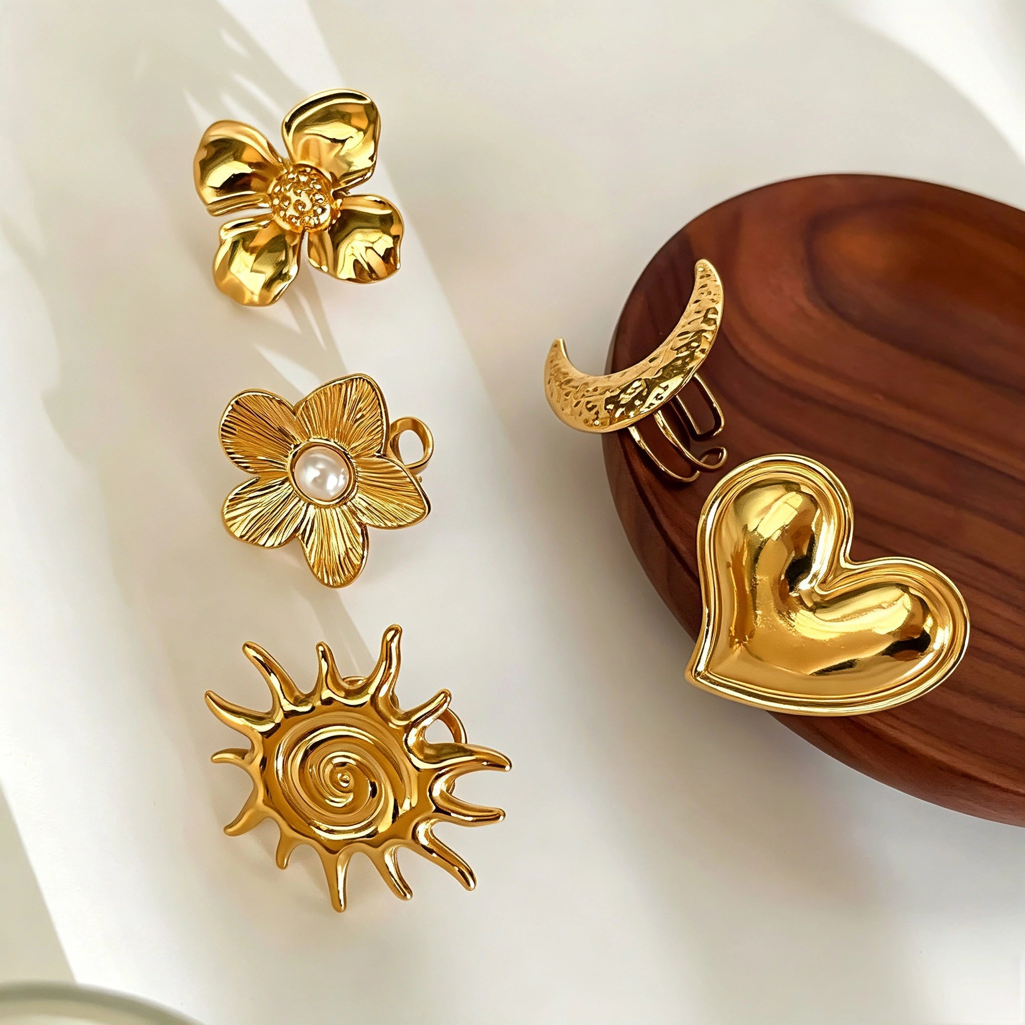 This 18K gold‑plated stainless steel ring set features bold sculpted designs of flowers, a puffy heart, swirling sun, and hammered crescent moon. Some flower rings are accented with a lustrous faux pearl for extra vintage charm. These open adjustable statement rings deliver a chunky retro aesthetic for everyday and special‑occasion styling.