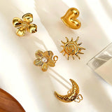 This 18K gold‑plated stainless steel ring set features bold sculpted designs of flowers, a puffy heart, swirling sun, and hammered crescent moon. Some flower rings are accented with a lustrous faux pearl for extra vintage charm. These open adjustable statement rings deliver a chunky retro aesthetic for everyday and special‑occasion styling.