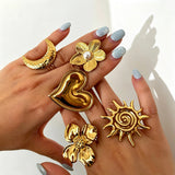 This 18K gold‑plated stainless steel ring set features bold sculpted designs of flowers, a puffy heart, swirling sun, and hammered crescent moon. Some flower rings are accented with a lustrous faux pearl for extra vintage charm. These open adjustable statement rings deliver a chunky retro aesthetic for everyday and special‑occasion styling.