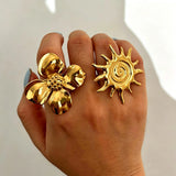 This 18K gold‑plated stainless steel ring set features bold sculpted designs of flowers, a puffy heart, swirling sun, and hammered crescent moon. Some flower rings are accented with a lustrous faux pearl for extra vintage charm. These open adjustable statement rings deliver a chunky retro aesthetic for everyday and special‑occasion styling.