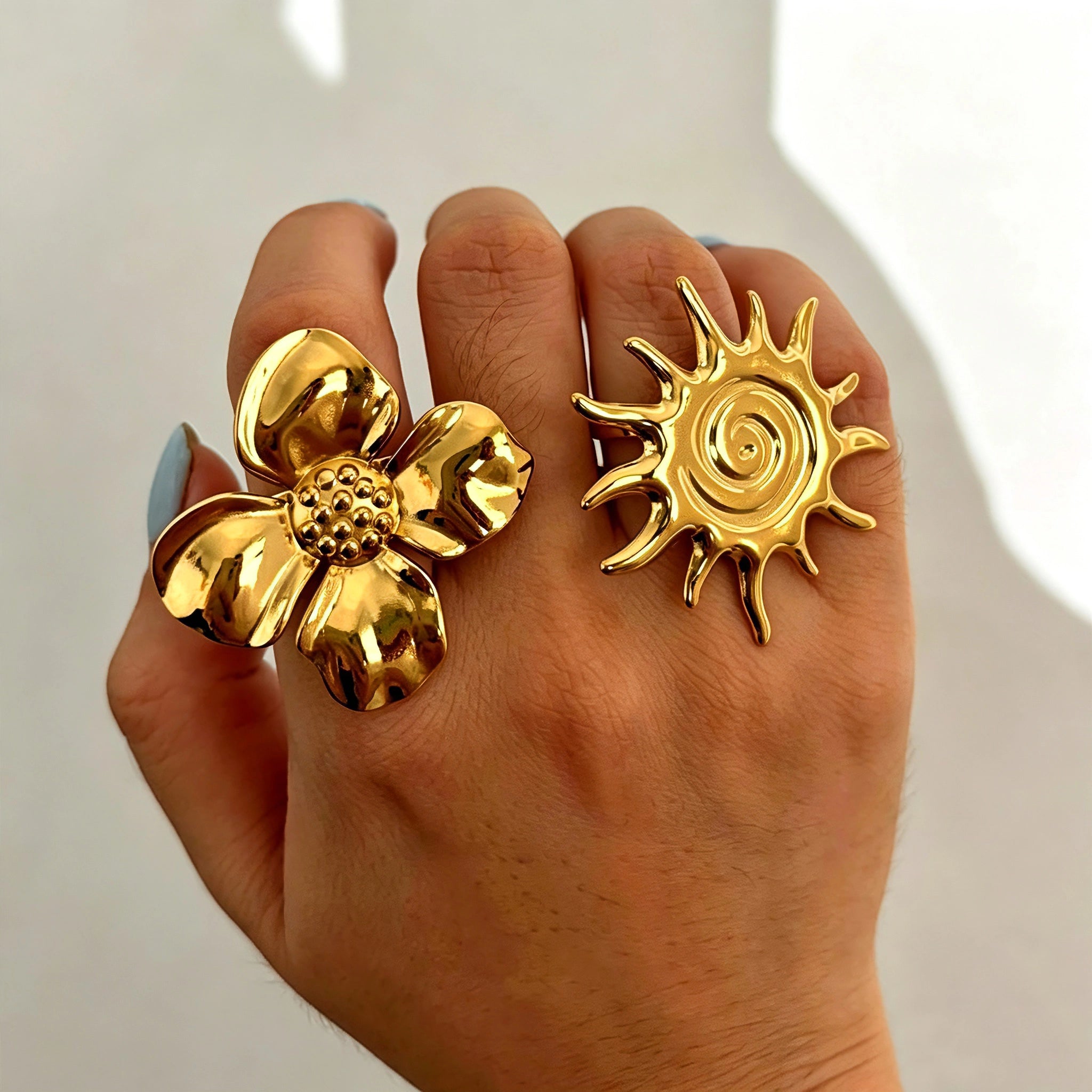 This 18K gold‑plated stainless steel ring set features bold sculpted designs of flowers, a puffy heart, swirling sun, and hammered crescent moon. Some flower rings are accented with a lustrous faux pearl for extra vintage charm. These open adjustable statement rings deliver a chunky retro aesthetic for everyday and special‑occasion styling.