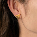 These thick 18K gold-plated stud earrings feature a sleek, modern curved triangle design with smooth, polished surfaces that catch the light beautifully. The sculpted, slightly concave shape creates a three-dimensional effect, adding subtle depth and dimension to the minimalist geometric silhouette.