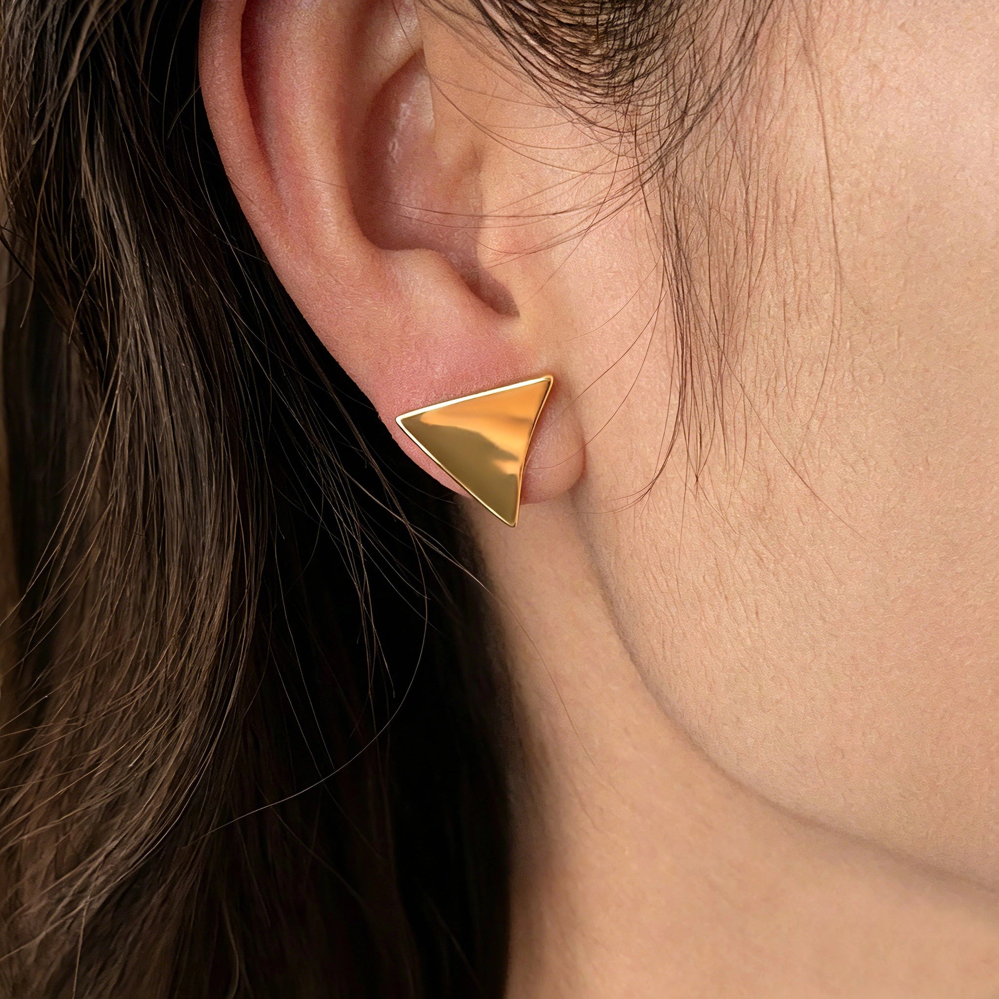 These thick 18K gold-plated stud earrings feature a sleek, modern curved triangle design with smooth, polished surfaces that catch the light beautifully. The sculpted, slightly concave shape creates a three-dimensional effect, adding subtle depth and dimension to the minimalist geometric silhouette.