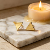 These thick 18K gold-plated stud earrings feature a sleek, modern curved triangle design with smooth, polished surfaces that catch the light beautifully. The sculpted, slightly concave shape creates a three-dimensional effect, adding subtle depth and dimension to the minimalist geometric silhouette.
