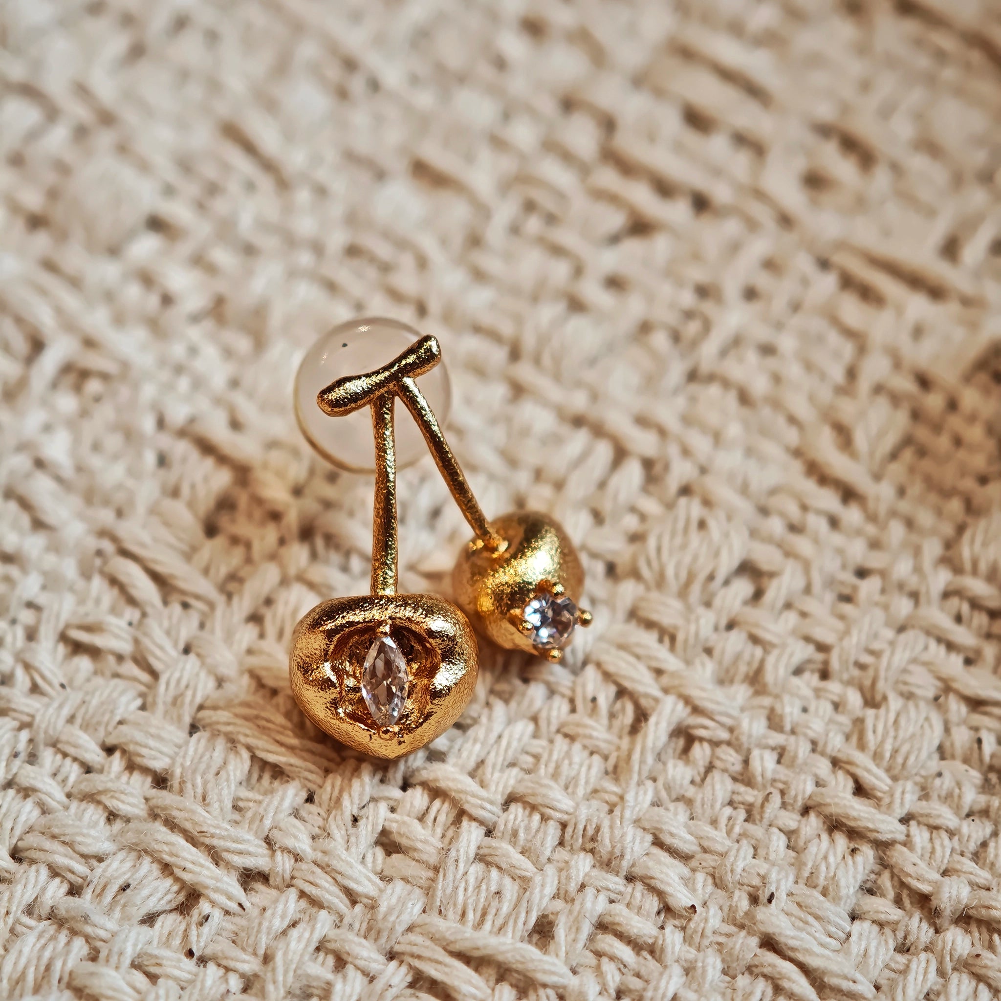 These cherry-shaped stud earrings feature a luxurious matte sandblasted finish, crafted from thick-plated real gold over 925 sterling silver posts. Each earring is designed as a pair of cherries, adorned with a marquise-cut and a round-cut sparkling clear stone, adding a delicate, eye-catching sparkle. The playful, organic cherry silhouette and premium gold plating make them a chic, elegant accessory for everyday wear.