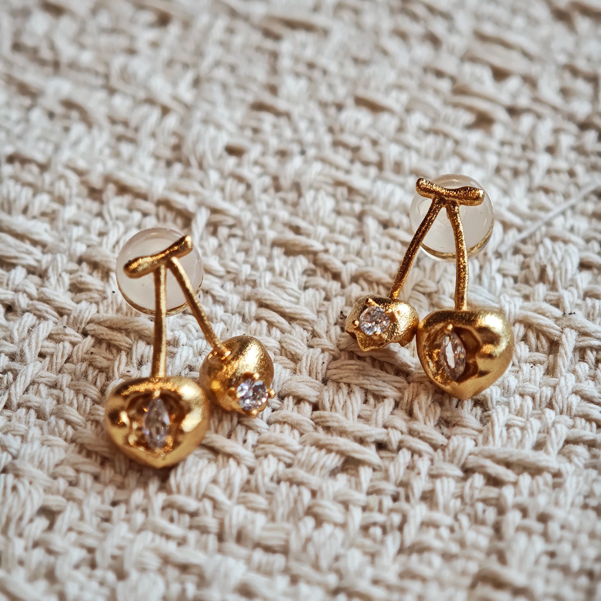 These cherry-shaped stud earrings feature a luxurious matte sandblasted finish, crafted from thick-plated real gold over 925 sterling silver posts. Each earring is designed as a pair of cherries, adorned with a marquise-cut and a round-cut sparkling clear stone, adding a delicate, eye-catching sparkle. The playful, organic cherry silhouette and premium gold plating make them a chic, elegant accessory for everyday wear.