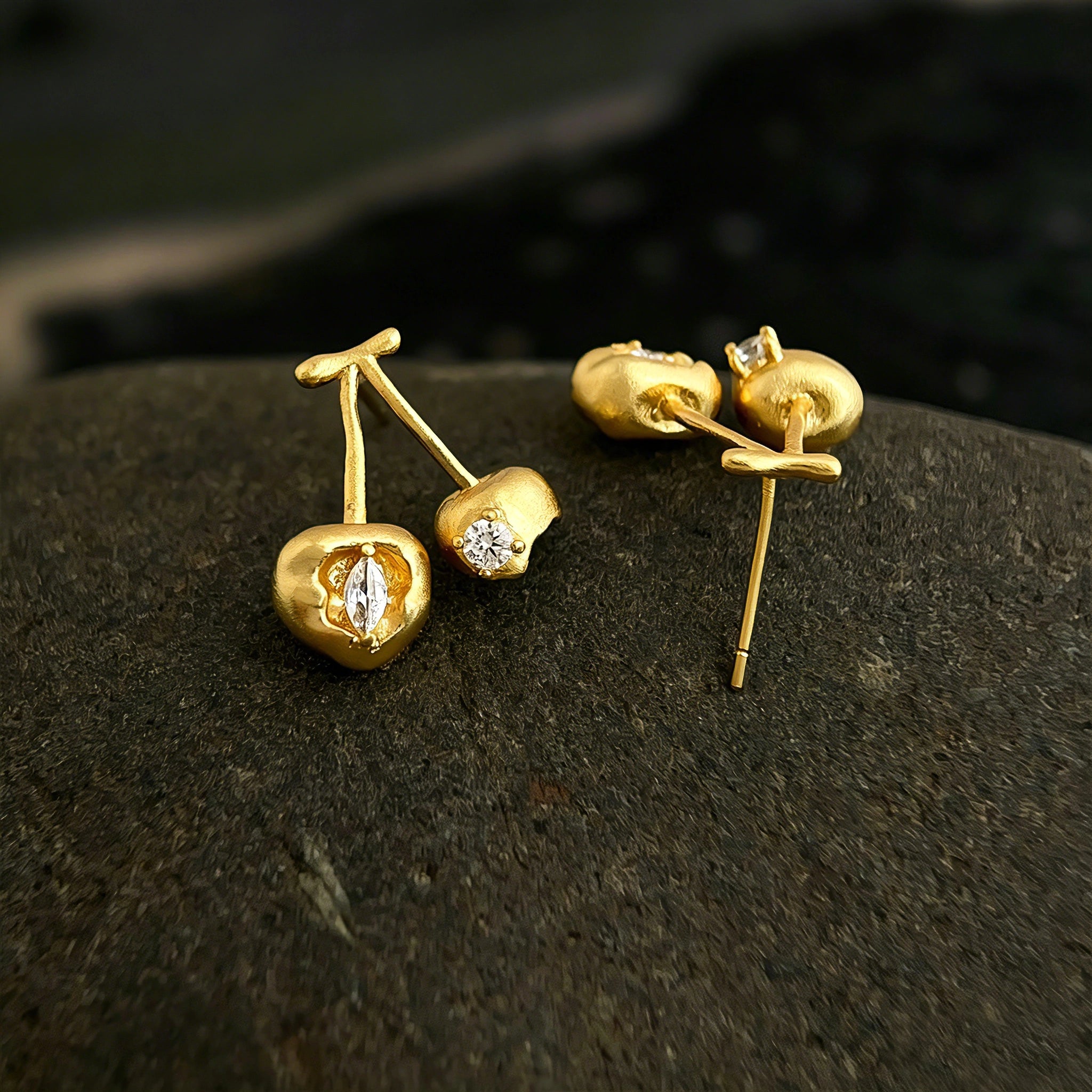 These cherry-shaped stud earrings feature a luxurious matte sandblasted finish, crafted from thick-plated real gold over 925 sterling silver posts. Each earring is designed as a pair of cherries, adorned with a marquise-cut and a round-cut sparkling clear stone, adding a delicate, eye-catching sparkle. The playful, organic cherry silhouette and premium gold plating make them a chic, elegant accessory for everyday wear.
