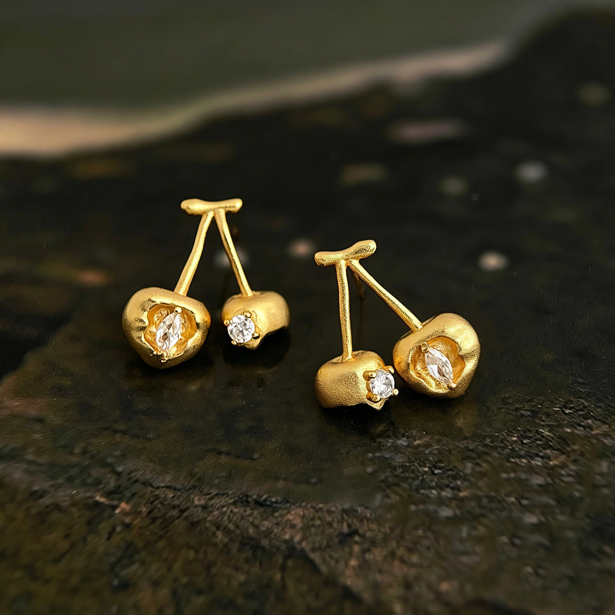 These cherry-shaped stud earrings feature a luxurious matte sandblasted finish, crafted from thick-plated real gold over 925 sterling silver posts. Each earring is designed as a pair of cherries, adorned with a marquise-cut and a round-cut sparkling clear stone, adding a delicate, eye-catching sparkle. The playful, organic cherry silhouette and premium gold plating make them a chic, elegant accessory for everyday wear.