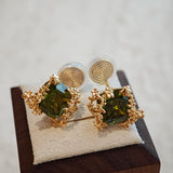 These stud earrings feature cushion-cut olive-green cubic zirconia stones, each encircled by delicate, nature-inspired gold floral and vine detailing. The thick 18K gold plating lends a rich, warm luster, contrasting beautifully with the deep green cubic zirconia to create an elegant, botanical aesthetic.