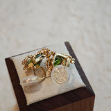 These stud earrings feature cushion-cut olive-green cubic zirconia stones, each encircled by delicate, nature-inspired gold floral and vine detailing. The thick 18K gold plating lends a rich, warm luster, contrasting beautifully with the deep green cubic zirconia to create an elegant, botanical aesthetic.