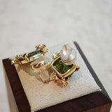 These stud earrings feature cushion-cut olive-green cubic zirconia stones, each encircled by delicate, nature-inspired gold floral and vine detailing. The thick 18K gold plating lends a rich, warm luster, contrasting beautifully with the deep green cubic zirconia to create an elegant, botanical aesthetic.
