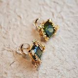These stud earrings feature cushion-cut olive-green cubic zirconia stones, each encircled by delicate, nature-inspired gold floral and vine detailing. The thick 18K gold plating lends a rich, warm luster, contrasting beautifully with the deep green cubic zirconia to create an elegant, botanical aesthetic.