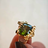 These stud earrings feature cushion-cut olive-green cubic zirconia stones, each encircled by delicate, nature-inspired gold floral and vine detailing. The thick 18K gold plating lends a rich, warm luster, contrasting beautifully with the deep green cubic zirconia to create an elegant, botanical aesthetic.