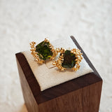 These stud earrings feature cushion-cut olive-green cubic zirconia stones, each encircled by delicate, nature-inspired gold floral and vine detailing. The thick 18K gold plating lends a rich, warm luster, contrasting beautifully with the deep green cubic zirconia to create an elegant, botanical aesthetic.