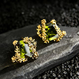 These stud earrings feature cushion-cut olive-green cubic zirconia stones, each encircled by delicate, nature-inspired gold floral and vine detailing. The thick 18K gold plating lends a rich, warm luster, contrasting beautifully with the deep green cubic zirconia to create an elegant, botanical aesthetic.