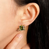 These stud earrings feature cushion-cut olive-green cubic zirconia stones, each encircled by delicate, nature-inspired gold floral and vine detailing. The thick 18K gold plating lends a rich, warm luster, contrasting beautifully with the deep green cubic zirconia to create an elegant, botanical aesthetic.