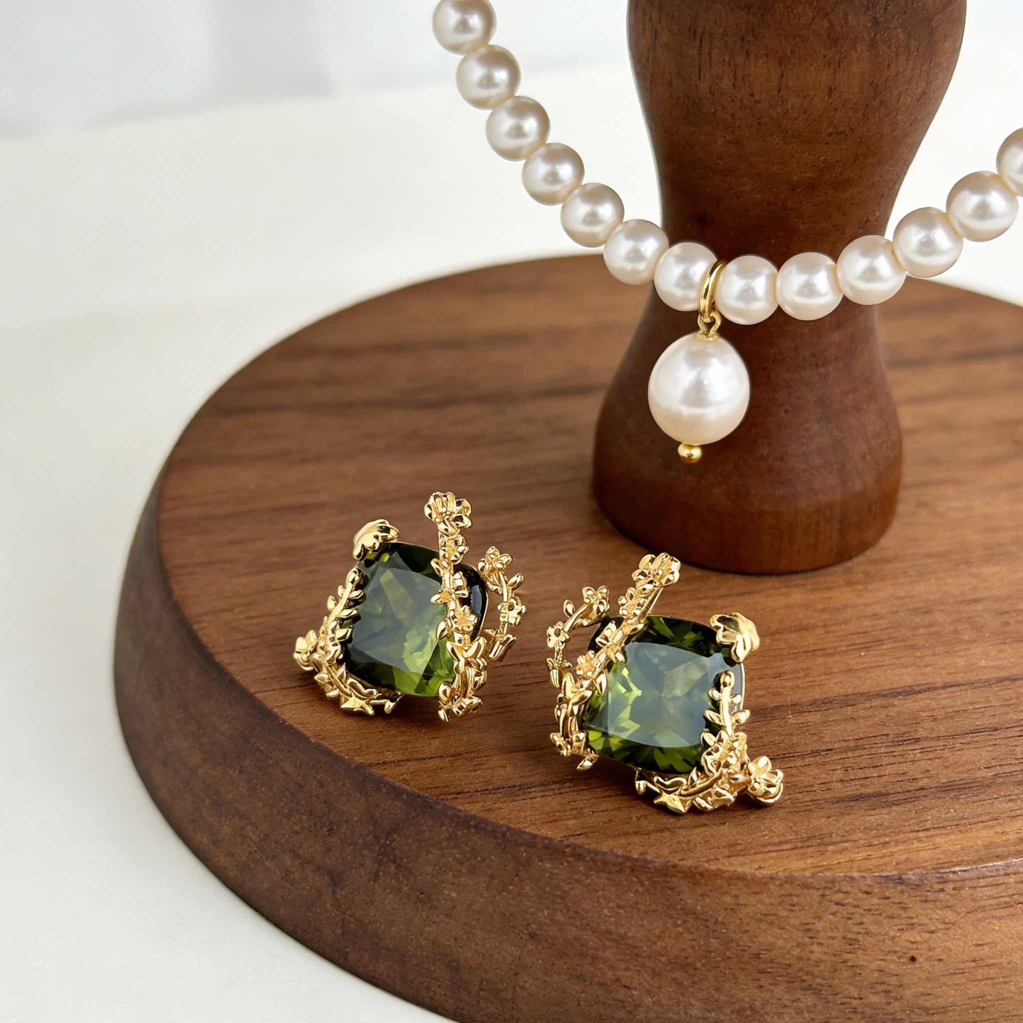 These stud earrings feature cushion-cut olive-green cubic zirconia stones, each encircled by delicate, nature-inspired gold floral and vine detailing. The thick 18K gold plating lends a rich, warm luster, contrasting beautifully with the deep green cubic zirconia to create an elegant, botanical aesthetic.