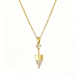 This is a necklace featuring a unique shovel-shaped pendant crafted with thick 18K gold plating, exuding a luxurious golden luster. The pendant is adorned with delicate micro-paved cubic zirconia stones, which sparkle brightly against the gold surface. Designed as a dainty pendant necklace, it showcases a sleek, minimalist style with intricate detailing on the shovel head and handle.