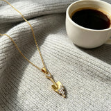 This is a necklace featuring a unique shovel-shaped pendant crafted with thick 18K gold plating, exuding a luxurious golden luster. The pendant is adorned with delicate micro-paved cubic zirconia stones, which sparkle brightly against the gold surface. Designed as a dainty pendant necklace, it showcases a sleek, minimalist style with intricate detailing on the shovel head and handle.
