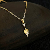 This is a necklace featuring a unique shovel-shaped pendant crafted with thick 18K gold plating, exuding a luxurious golden luster. The pendant is adorned with delicate micro-paved cubic zirconia stones, which sparkle brightly against the gold surface. Designed as a dainty pendant necklace, it showcases a sleek, minimalist style with intricate detailing on the shovel head and handle.