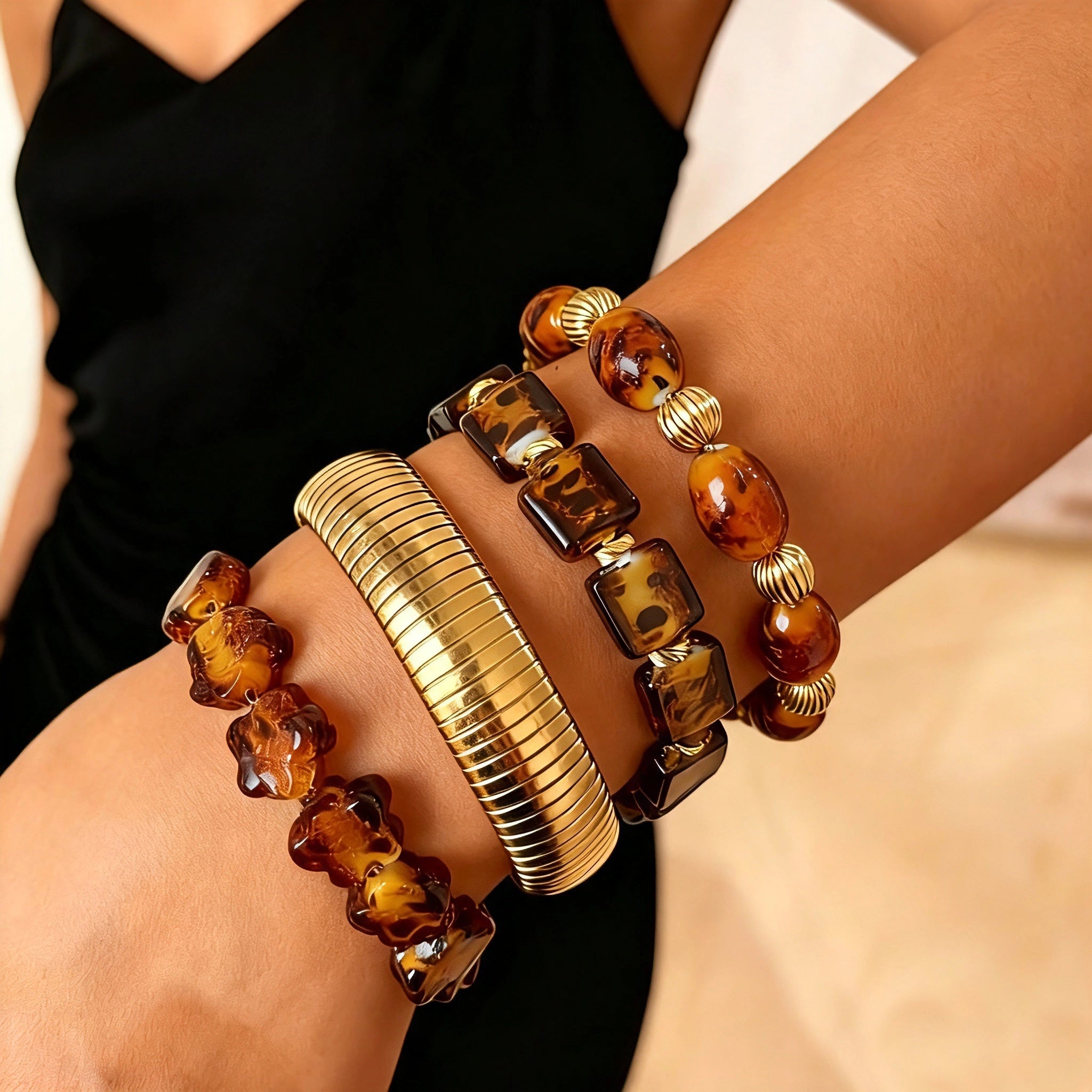 This 4-piece stackable bracelet set blends glossy tortoiseshell-pattern glass beads with polished stainless steel hardware. It includes flower-shaped, square, and oval beaded bracelets paired with a flexible gold-tone ribbed bangle. Perfect for layered styling, these warm earthy-toned accessories effortlessly elevate everyday and evening outfits.