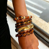This 4-piece stackable bracelet set blends glossy tortoiseshell-pattern glass beads with polished stainless steel hardware. It includes flower-shaped, square, and oval beaded bracelets paired with a flexible gold-tone ribbed bangle. Perfect for layered styling, these warm earthy-toned accessories effortlessly elevate everyday and evening outfits.