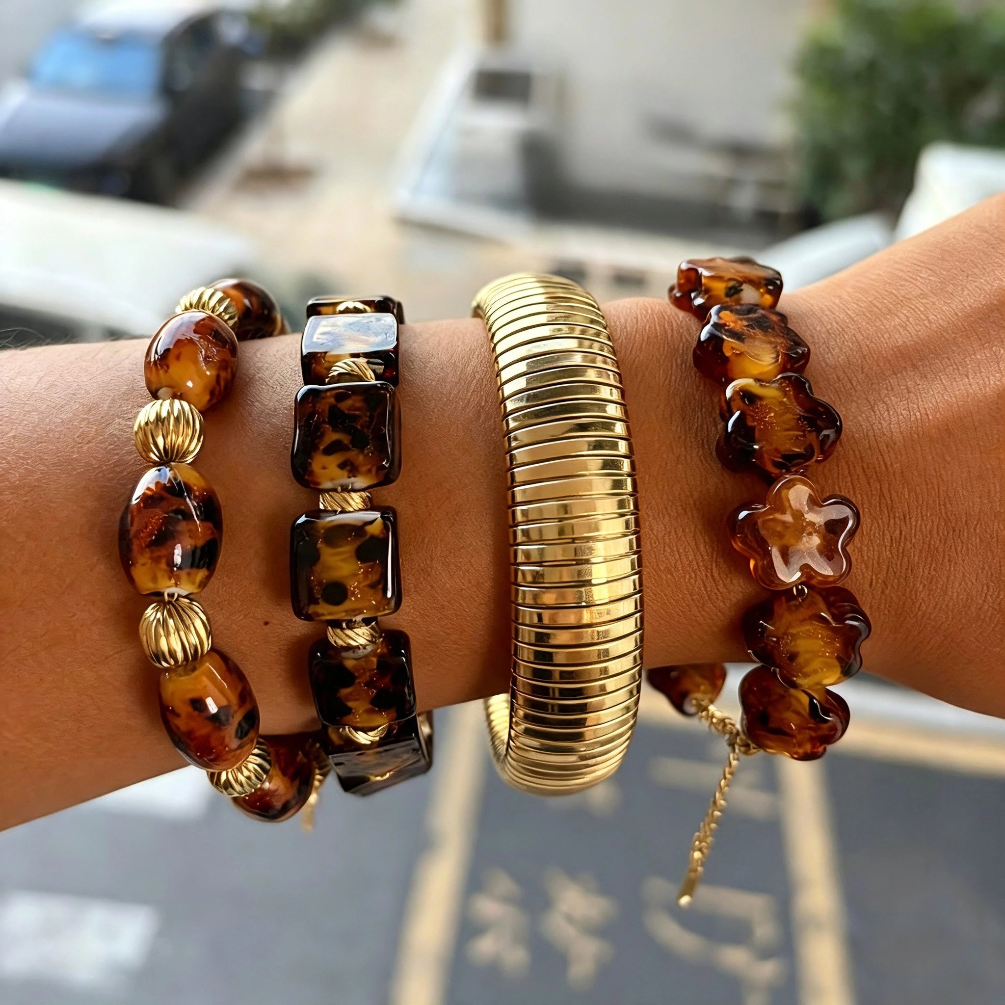 This 4-piece stackable bracelet set blends glossy tortoiseshell-pattern glass beads with polished stainless steel hardware. It includes flower-shaped, square, and oval beaded bracelets paired with a flexible gold-tone ribbed bangle. Perfect for layered styling, these warm earthy-toned accessories effortlessly elevate everyday and evening outfits.