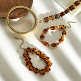 This 4-piece stackable bracelet set blends glossy tortoiseshell-pattern glass beads with polished stainless steel hardware. It includes flower-shaped, square, and oval beaded bracelets paired with a flexible gold-tone ribbed bangle. Perfect for layered styling, these warm earthy-toned accessories effortlessly elevate everyday and evening outfits.