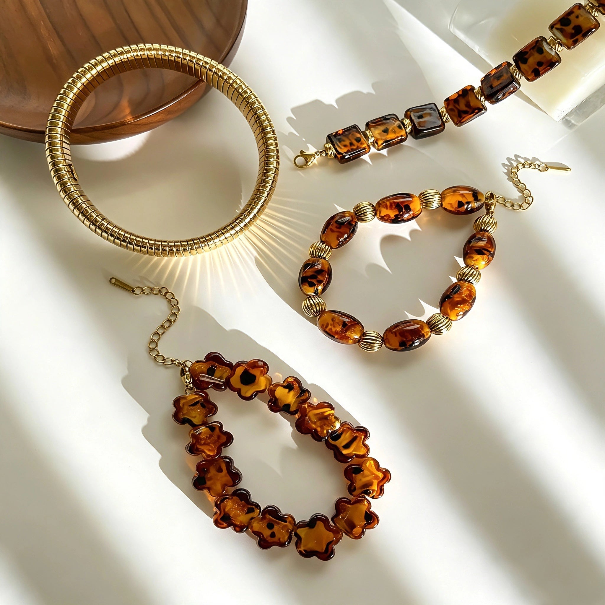 This 4-piece stackable bracelet set blends glossy tortoiseshell-pattern glass beads with polished stainless steel hardware. It includes flower-shaped, square, and oval beaded bracelets paired with a flexible gold-tone ribbed bangle. Perfect for layered styling, these warm earthy-toned accessories effortlessly elevate everyday and evening outfits.