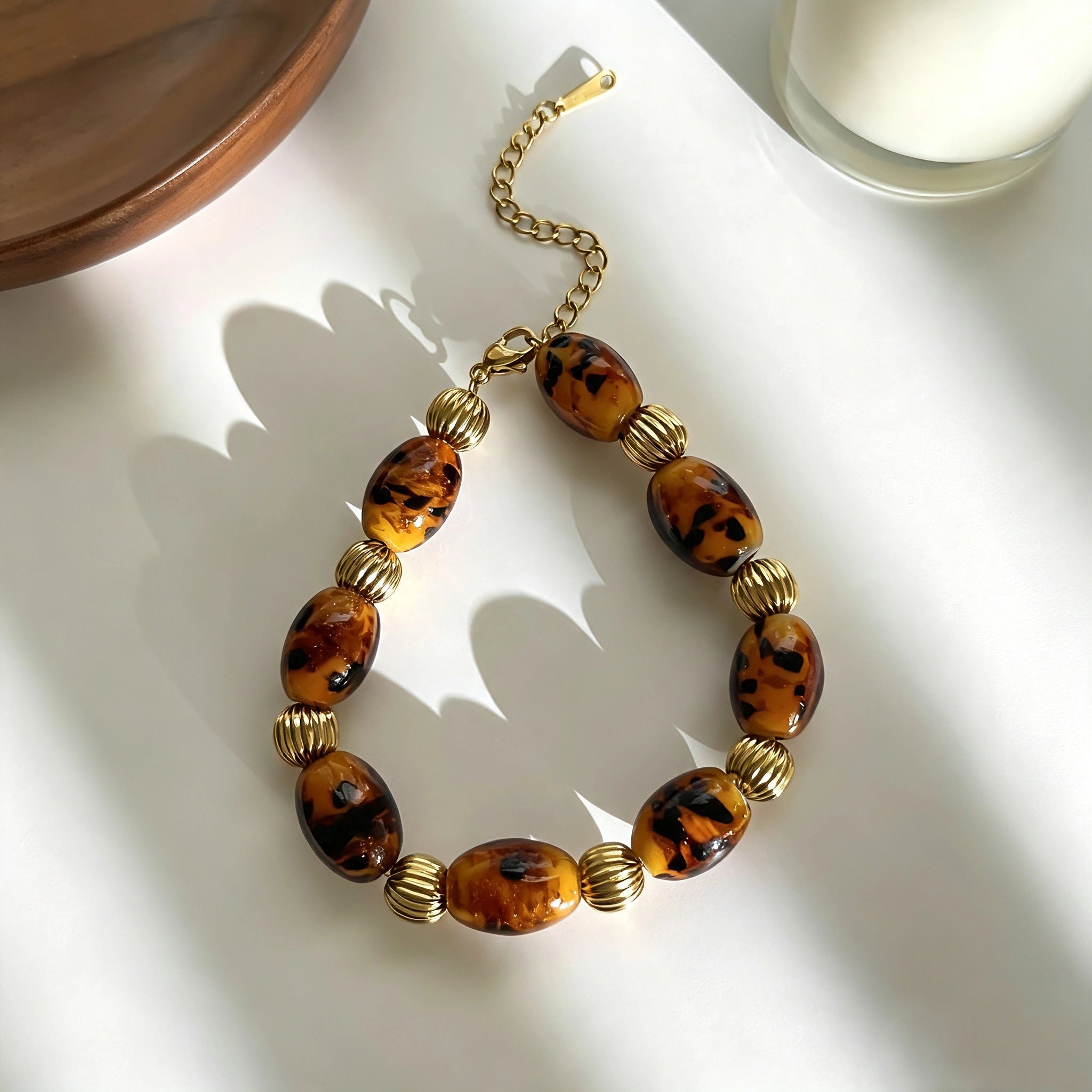 This 4-piece stackable bracelet set blends glossy tortoiseshell-pattern glass beads with polished stainless steel hardware. It includes flower-shaped, square, and oval beaded bracelets paired with a flexible gold-tone ribbed bangle. Perfect for layered styling, these warm earthy-toned accessories effortlessly elevate everyday and evening outfits.