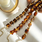 This 4-piece stackable bracelet set blends glossy tortoiseshell-pattern glass beads with polished stainless steel hardware. It includes flower-shaped, square, and oval beaded bracelets paired with a flexible gold-tone ribbed bangle. Perfect for layered styling, these warm earthy-toned accessories effortlessly elevate everyday and evening outfits.