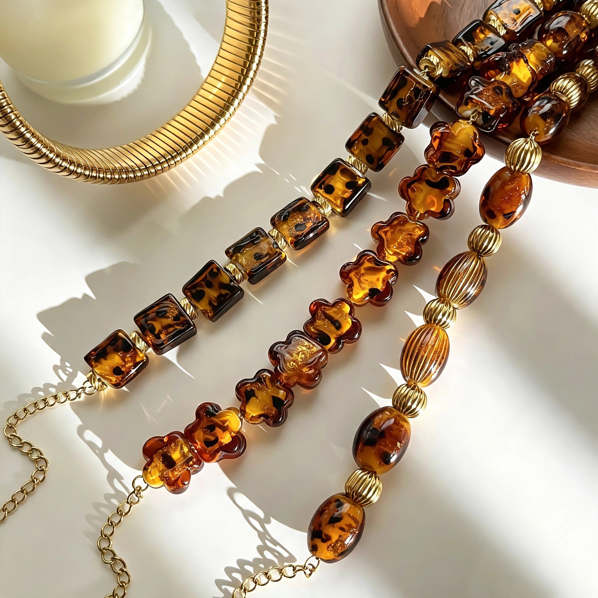 This 4-piece stackable bracelet set blends glossy tortoiseshell-pattern glass beads with polished stainless steel hardware. It includes flower-shaped, square, and oval beaded bracelets paired with a flexible gold-tone ribbed bangle. Perfect for layered styling, these warm earthy-toned accessories effortlessly elevate everyday and evening outfits.