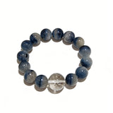 Blue rabbit hair and clear quartz beaded bracelet, featuring blue-gray rabbit hair quartz beads and a clear quartz focal bead, strung together in a circular design.