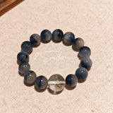 Blue rabbit hair and clear quartz beaded bracelet, featuring blue-gray rabbit hair quartz beads and a clear quartz focal bead, strung together in a circular design.