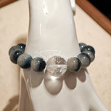 Blue rabbit hair and clear quartz beaded bracelet, featuring blue-gray rabbit hair quartz beads and a clear quartz focal bead, strung together in a circular design.