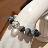 Blue rabbit hair and clear quartz beaded bracelet, featuring blue-gray rabbit hair quartz beads and a clear quartz focal bead, strung together in a circular design.