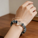 Blue rabbit hair and clear quartz beaded bracelet, featuring blue-gray rabbit hair quartz beads and a clear quartz focal bead, strung together in a circular design.
