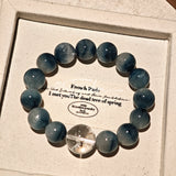 Blue rabbit hair and clear quartz beaded bracelet, featuring blue-gray rabbit hair quartz beads and a clear quartz focal bead, strung together in a circular design.