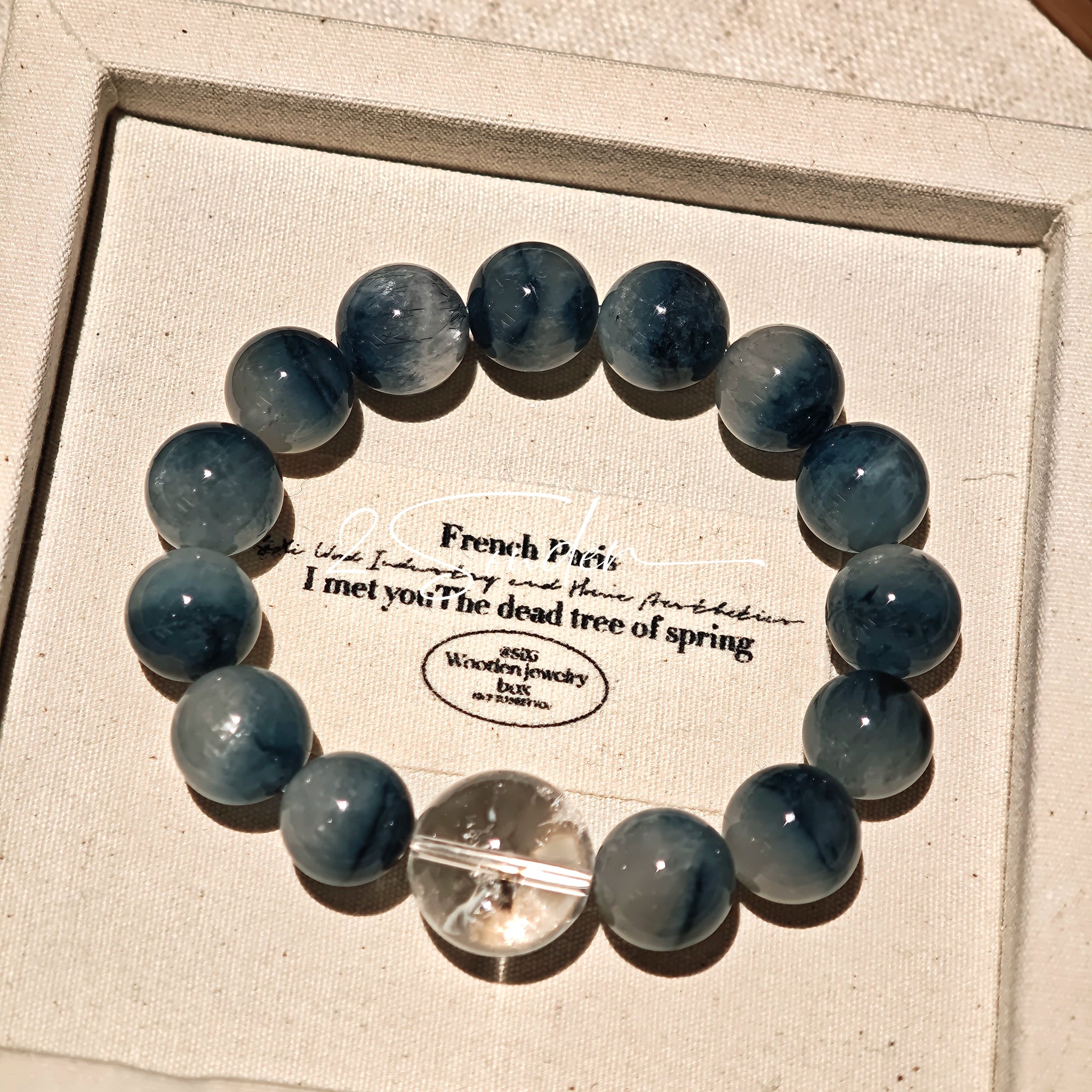 Blue rabbit hair and clear quartz beaded bracelet, featuring blue-gray rabbit hair quartz beads and a clear quartz focal bead, strung together in a circular design.