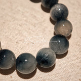 Blue rabbit hair and clear quartz beaded bracelet, featuring blue-gray rabbit hair quartz beads and a clear quartz focal bead, strung together in a circular design.