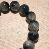 Blue rabbit hair and clear quartz beaded bracelet, featuring blue-gray rabbit hair quartz beads and a clear quartz focal bead, strung together in a circular design.