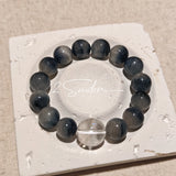 Blue rabbit hair and clear quartz beaded bracelet, featuring blue-gray rabbit hair quartz beads and a clear quartz focal bead, strung together in a circular design.