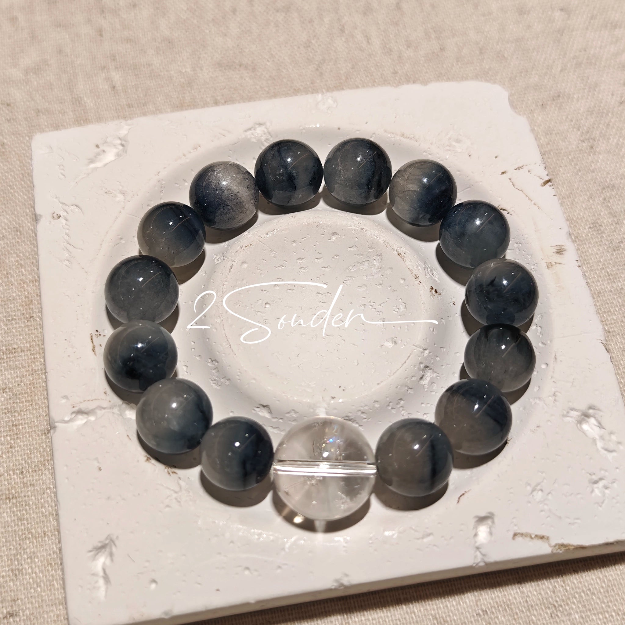 Blue rabbit hair and clear quartz beaded bracelet, featuring blue-gray rabbit hair quartz beads and a clear quartz focal bead, strung together in a circular design.