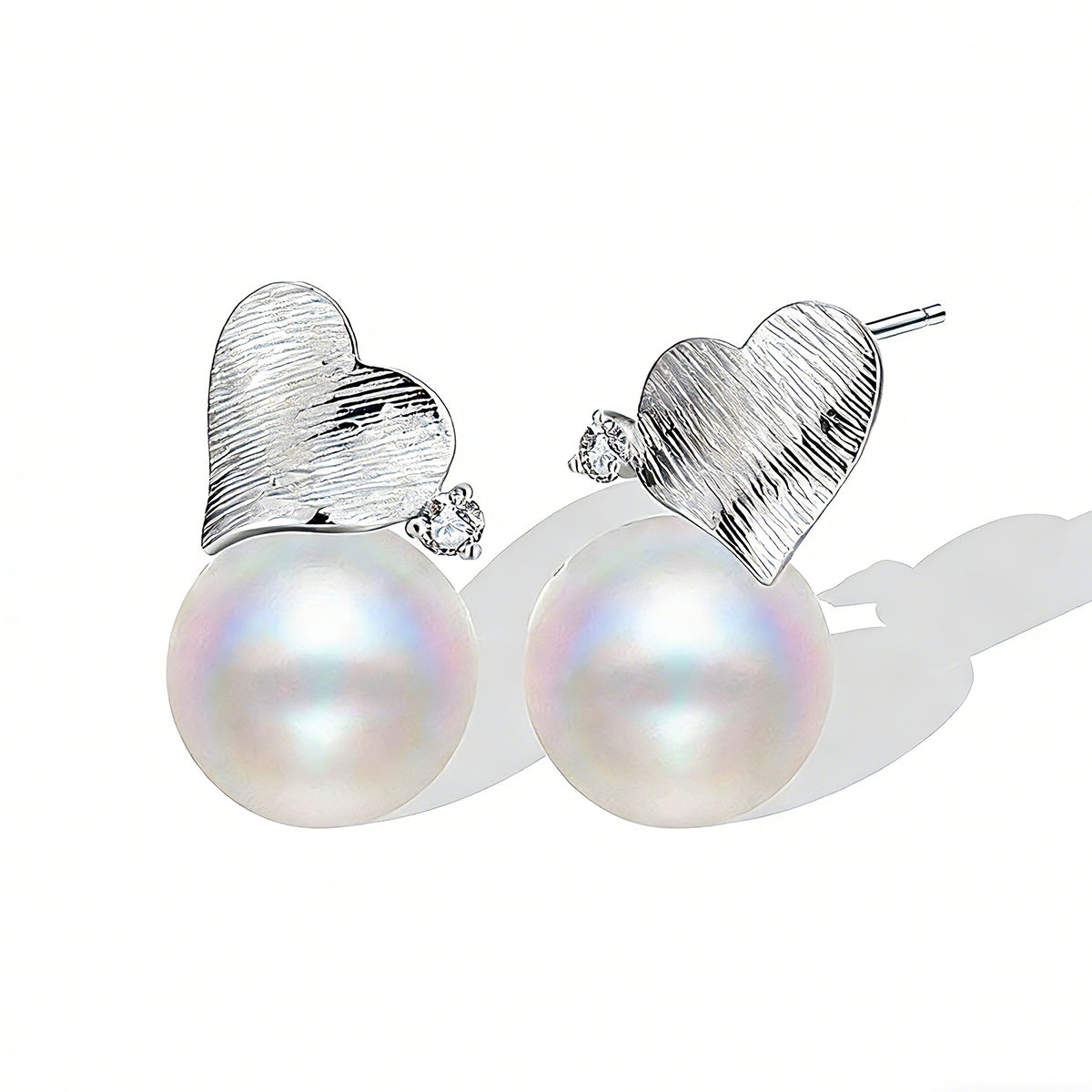 This minimalist pair of silver pearl stud earrings cleverly combine a chic silver heart-shaped pendant (11.7 mm wide) with a striking pearl teardrop (total height: 19.4 mm), with the pearl beneath the heart, creating a unique and stylish silhouette.