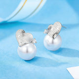 This minimalist pair of silver pearl stud earrings cleverly combine a chic silver heart-shaped pendant (11.7 mm wide) with a striking pearl teardrop (total height: 19.4 mm), with the pearl beneath the heart, creating a unique and stylish silhouette.