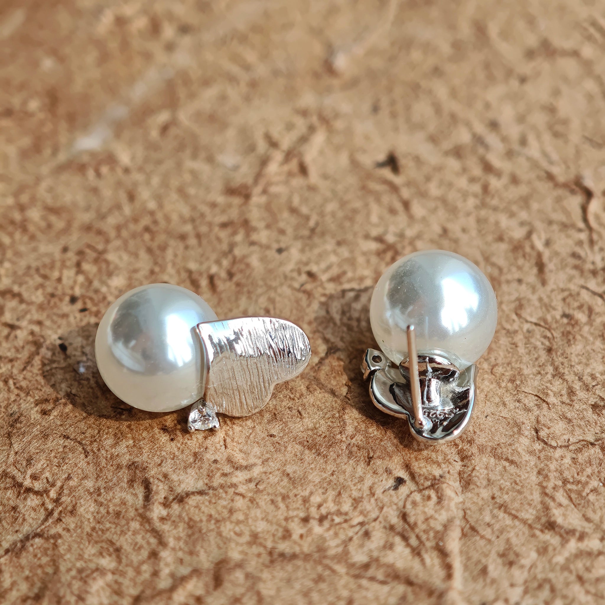 This minimalist pair of silver pearl stud earrings cleverly combine a chic silver heart-shaped pendant (11.7 mm wide) with a striking pearl teardrop (total height: 19.4 mm), with the pearl beneath the heart, creating a unique and stylish silhouette.