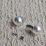 This minimalist pair of silver pearl stud earrings cleverly combine a chic silver heart-shaped pendant (11.7 mm wide) with a striking pearl teardrop (total height: 19.4 mm), with the pearl beneath the heart, creating a unique and stylish silhouette.