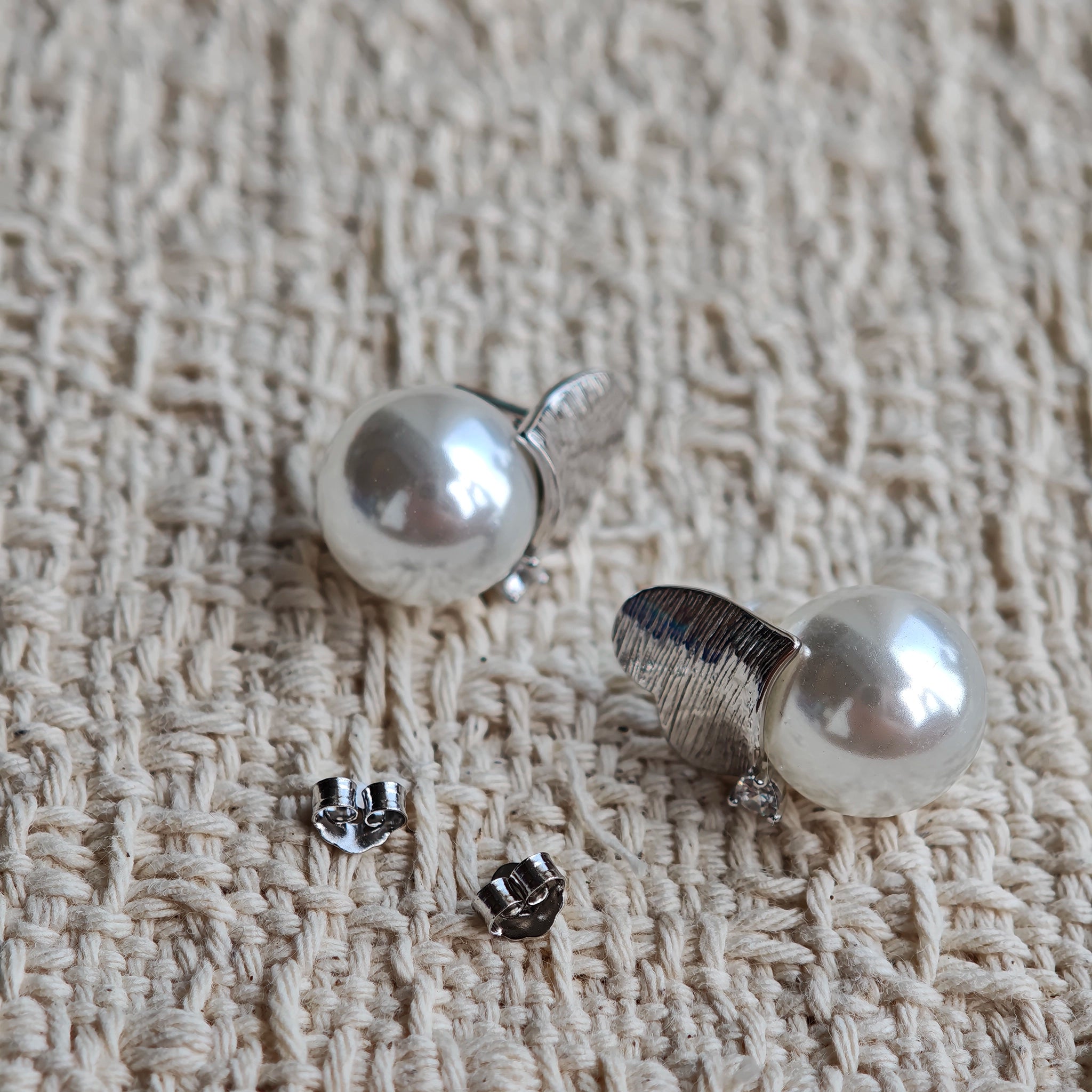 This minimalist pair of silver pearl stud earrings cleverly combine a chic silver heart-shaped pendant (11.7 mm wide) with a striking pearl teardrop (total height: 19.4 mm), with the pearl beneath the heart, creating a unique and stylish silhouette.