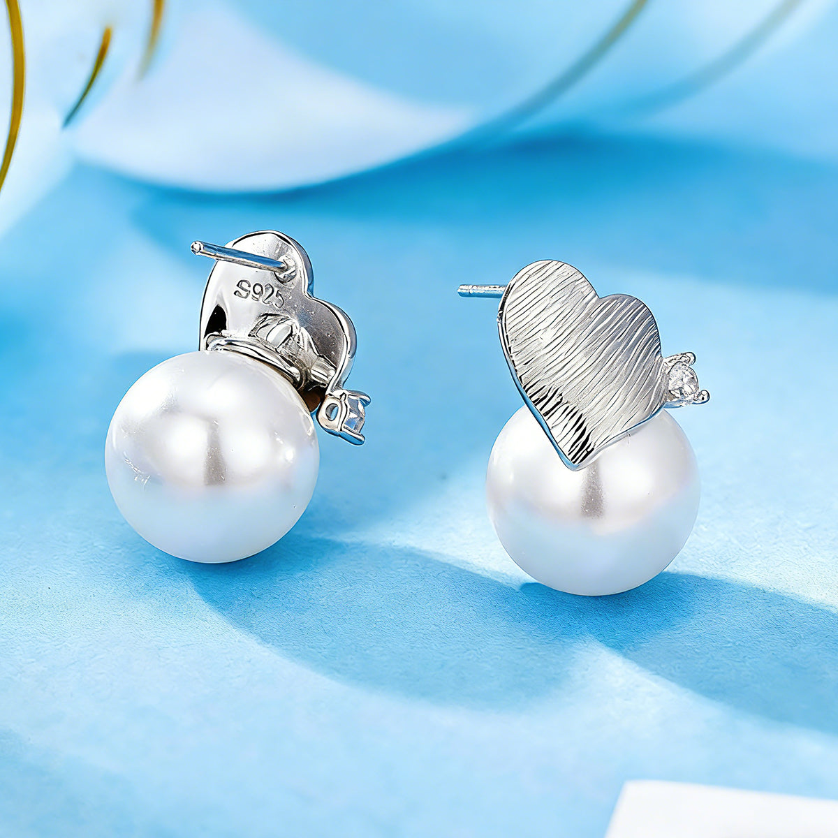 This minimalist pair of silver pearl stud earrings cleverly combine a chic silver heart-shaped pendant (11.7 mm wide) with a striking pearl teardrop (total height: 19.4 mm), with the pearl beneath the heart, creating a unique and stylish silhouette.